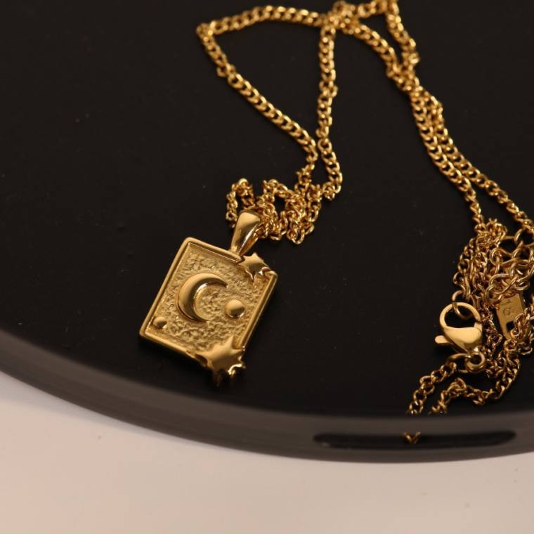 Gold-tone necklace with a square textured pendant embossed with a crescent moon, a dot and two eight-point stars