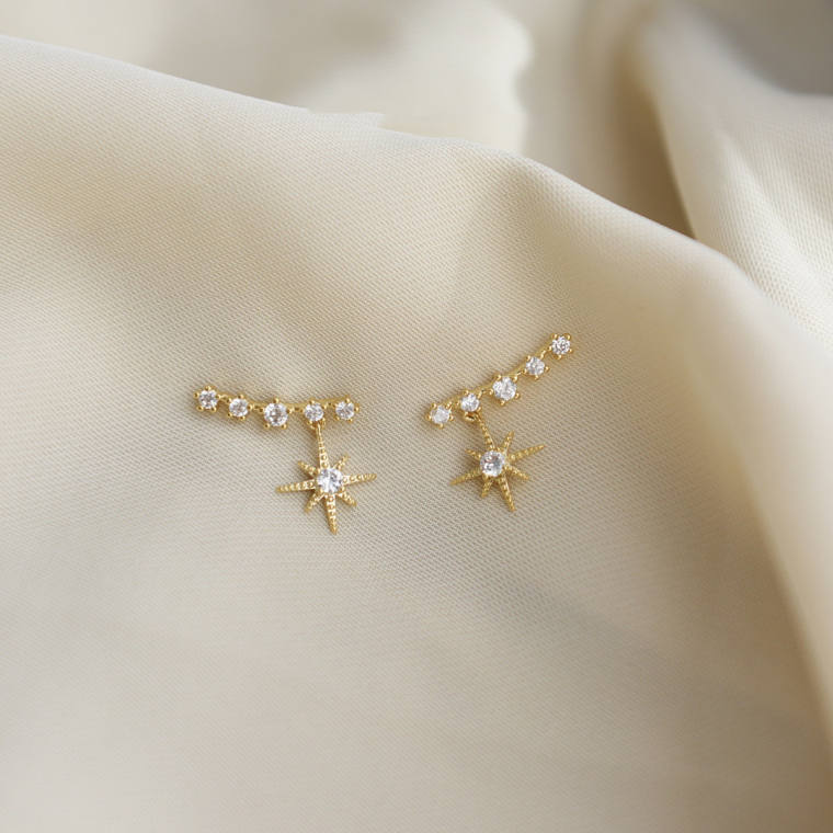 Gold-tone ear climber earring: an arc of five small clear stones following the ear, with a starburst charm hanging from one end