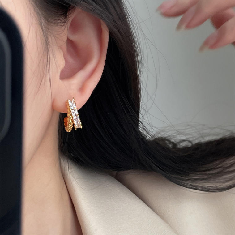 Open C-shaped hoop earring: a twisted rope-textured band crossed by a row of square clear stones