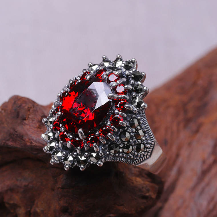 Cocktail ring with a large faceted red oval stone ringed by small red stones and a dark pavé border