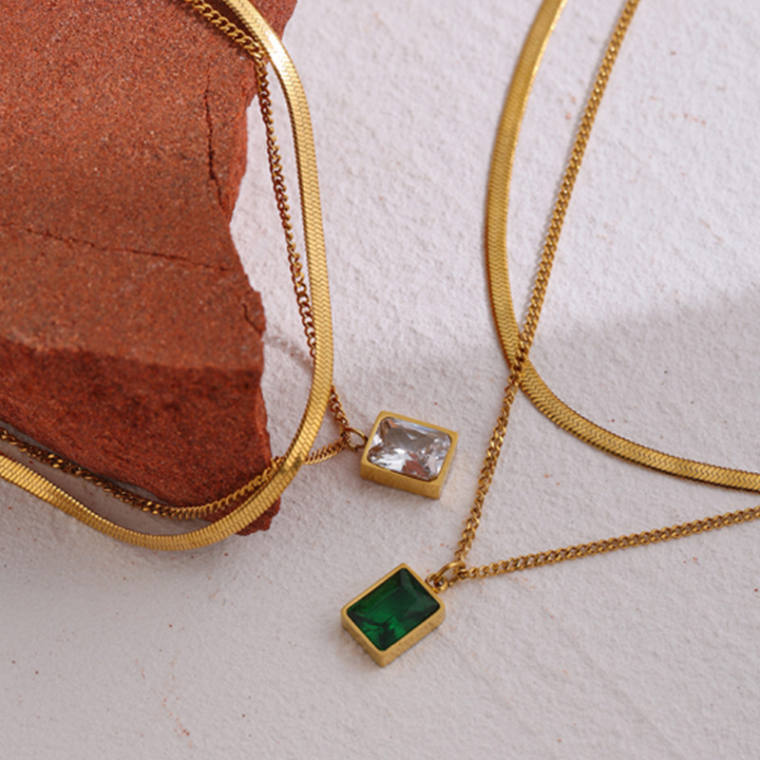 Two layered gold-tone chains, a flat snake chain and a fine curb chain with a square bezel-set stone pendant