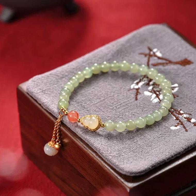 Bracelet of pale green beads with a small gold-capped gourd bead, one orange bead and a short gold-tone chain tassel