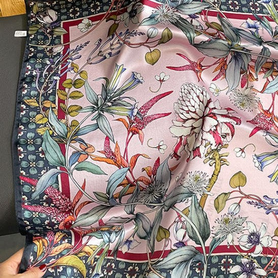 Square silk scarf printed with pink and white blooms on a pink ground inside a dark patterned border