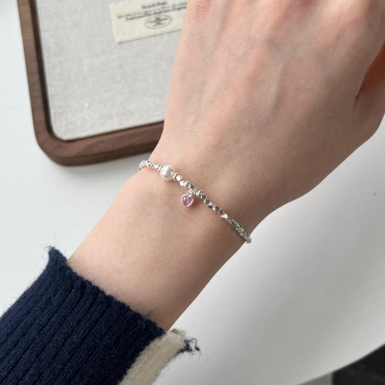 Bracelet of small faceted silver-tone beads with one round white bead and a small pink heart charm