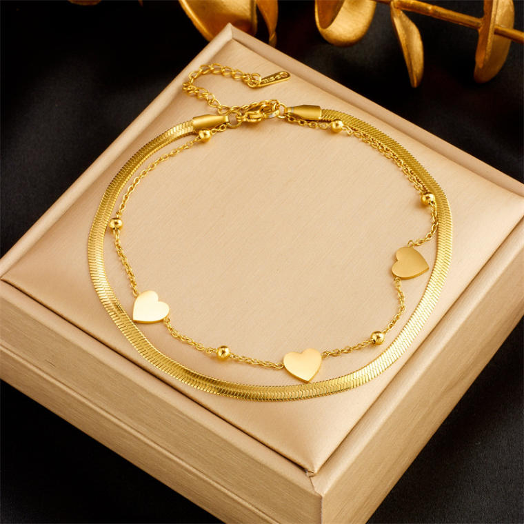 Double-layer gold-tone anklet shown in three styles: hearts on herringbone chain, sky-blue crackle beads, and tree charms with clear beads