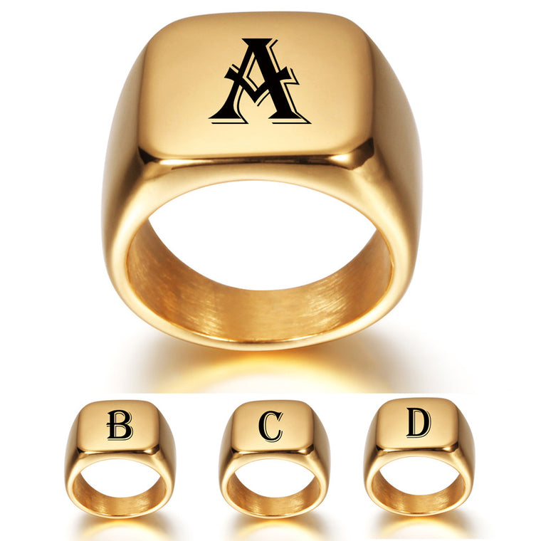 Chunky gold square signet ring with a single black letter across the flat face